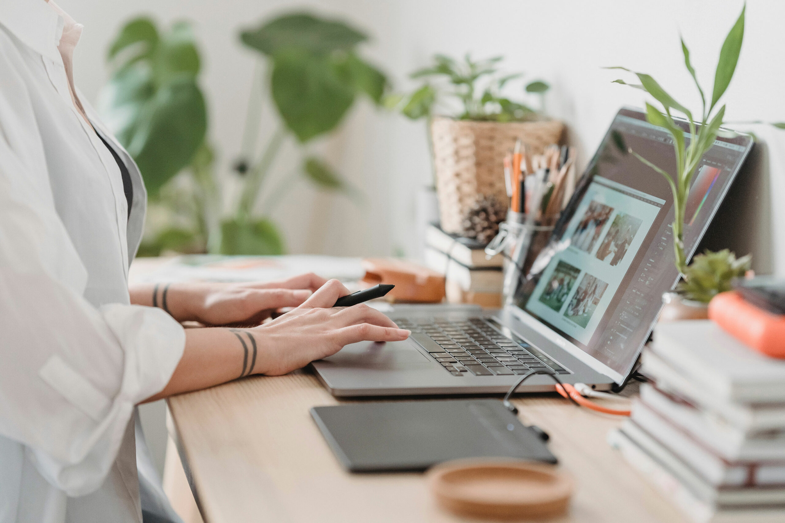 Mains sur le clavier d’un ordinateur portable qui affiche une maquette de site, sur un bureau entouré de plantes